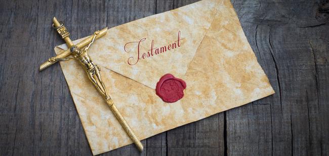 Goldene Kreuzfigur auf einem alten Testamentbriefumschlag mit rotem Wachsiegel auf einer Holzoberfläche.