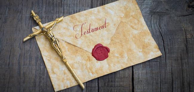 Goldene Kreuzfigur auf einem alten Testamentbriefumschlag mit rotem Wachsiegel auf einer Holzoberfläche.